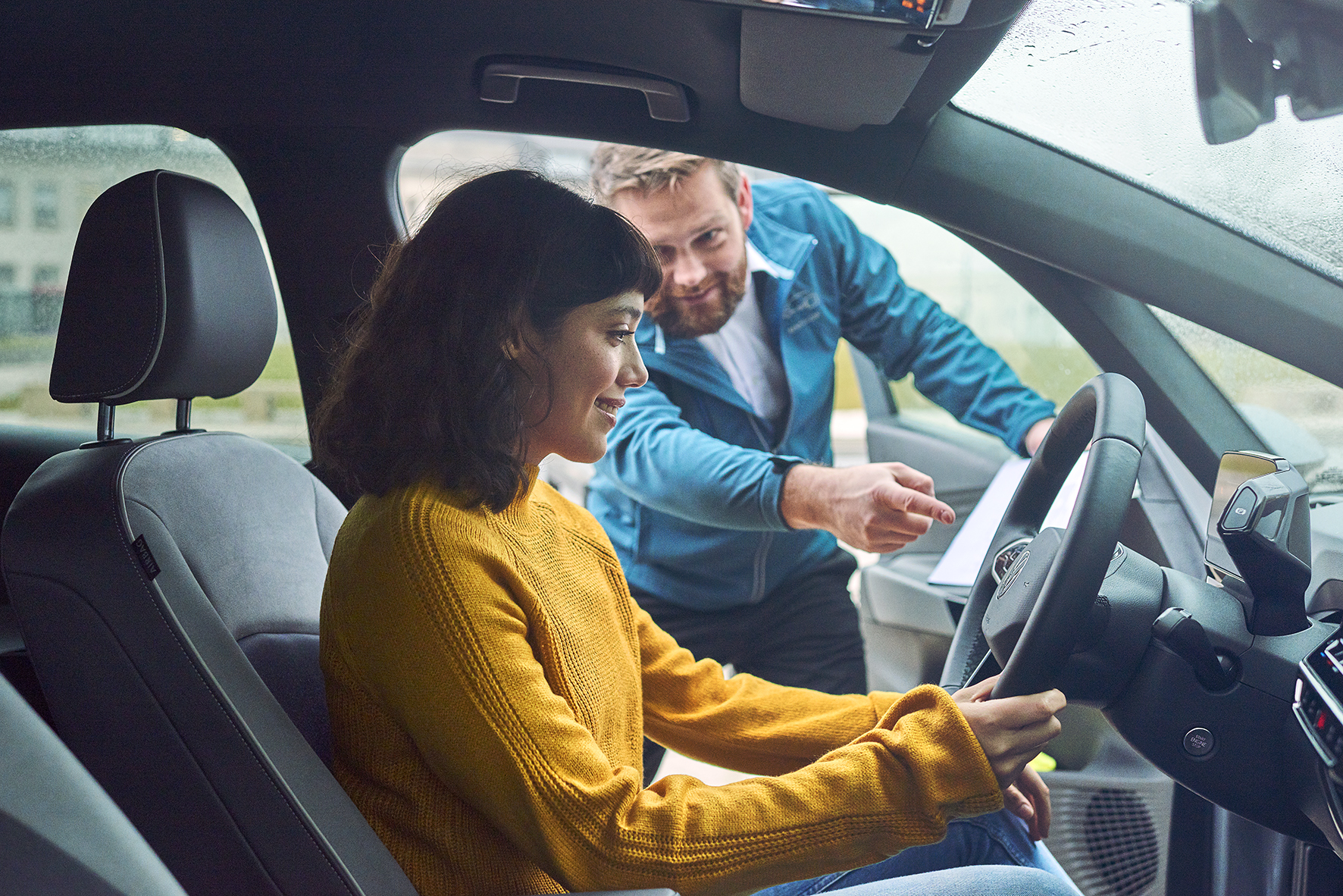 Vermietrepräsentantin der Autovermietung VW FS | Rent-a-Car erklärt einer im Auto sitzenden Kundin etwas