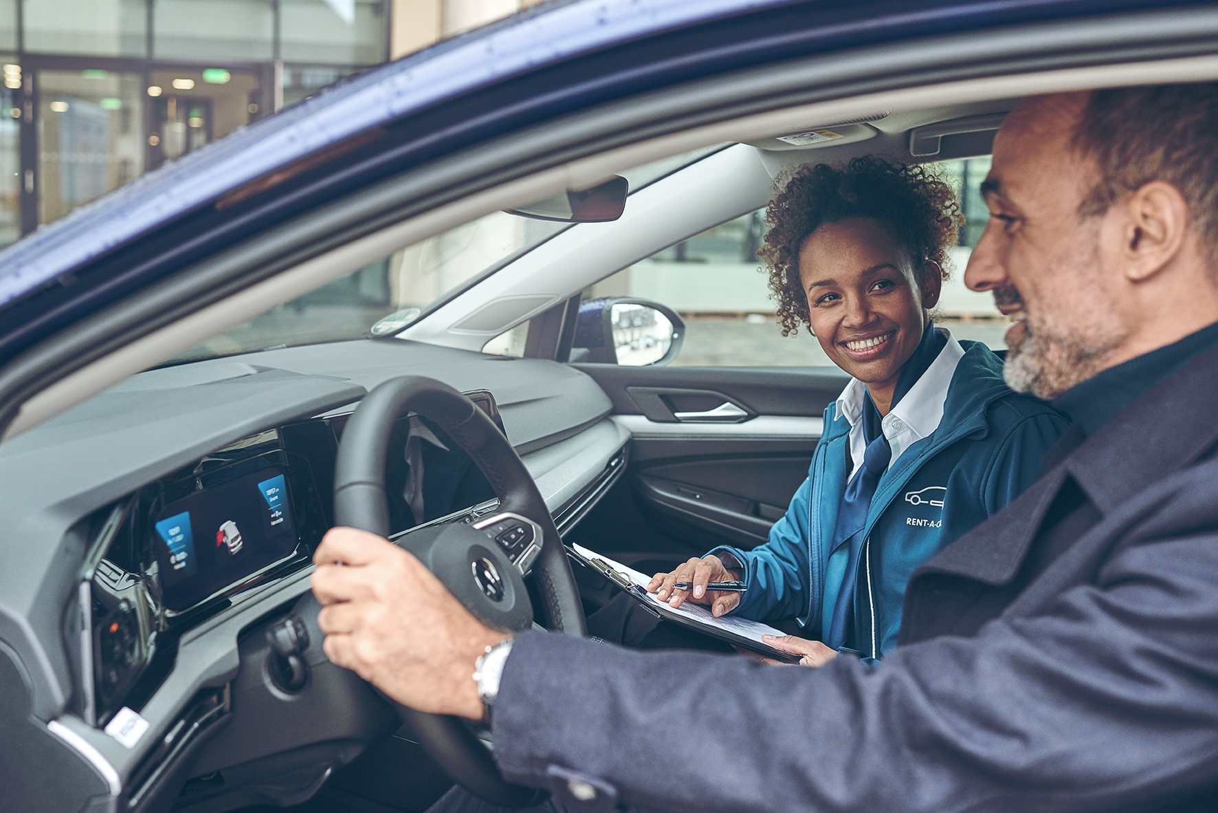 Vermietrepräsentantin der Autovermietung VW FS | Rent-a-Car sitzt mit einem Kunden in einem Mietwagen